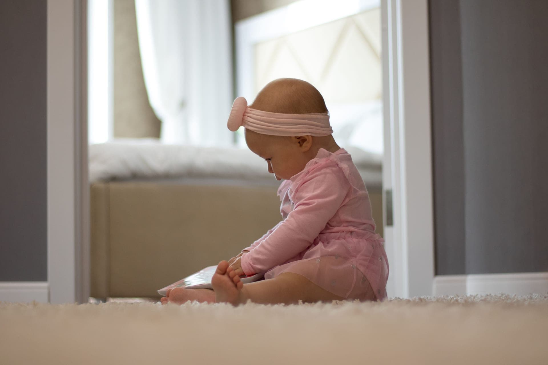 A baby sitting up on a rug, looking around a room
