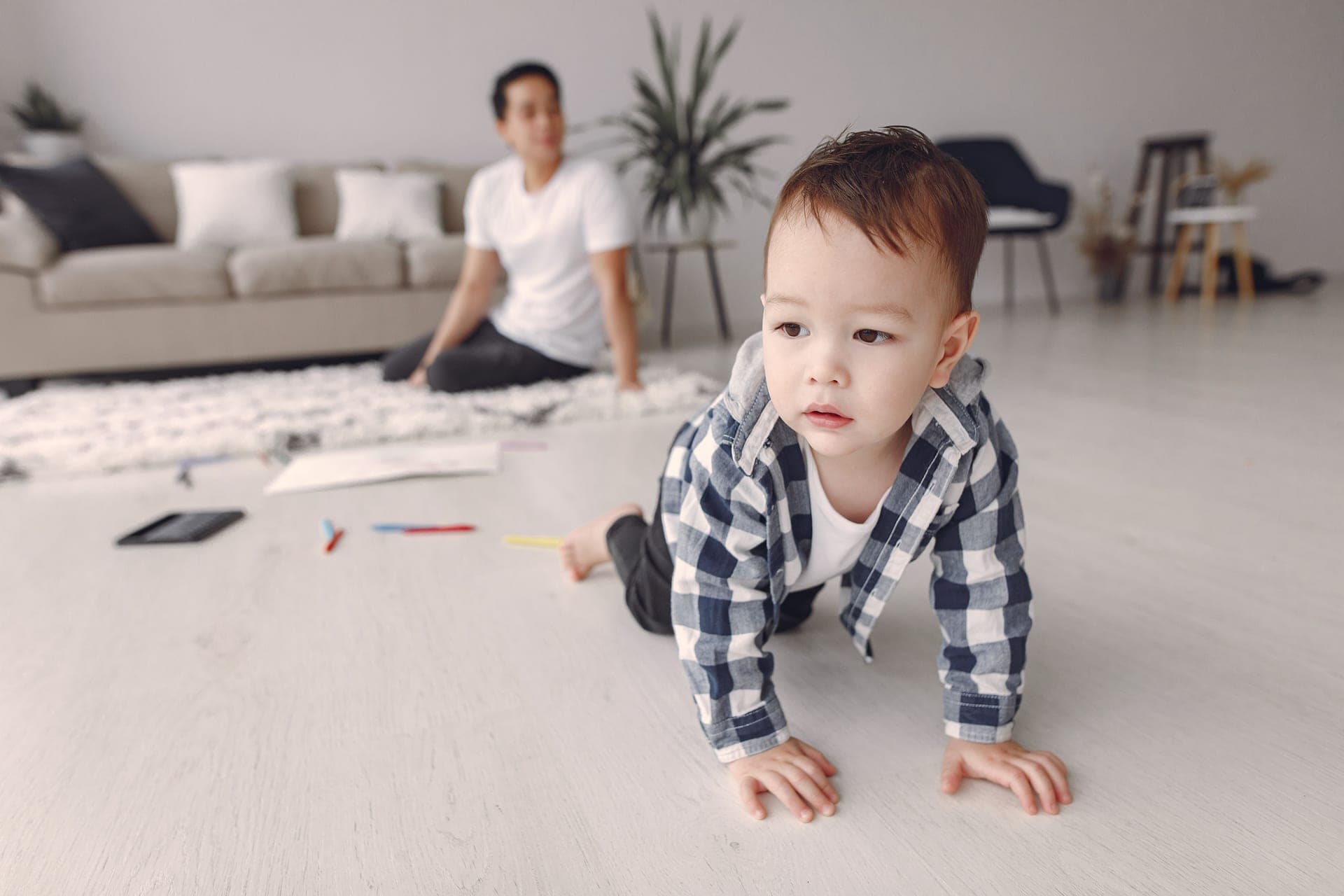 A parent sitting on the floor with a crawling baby in a living room