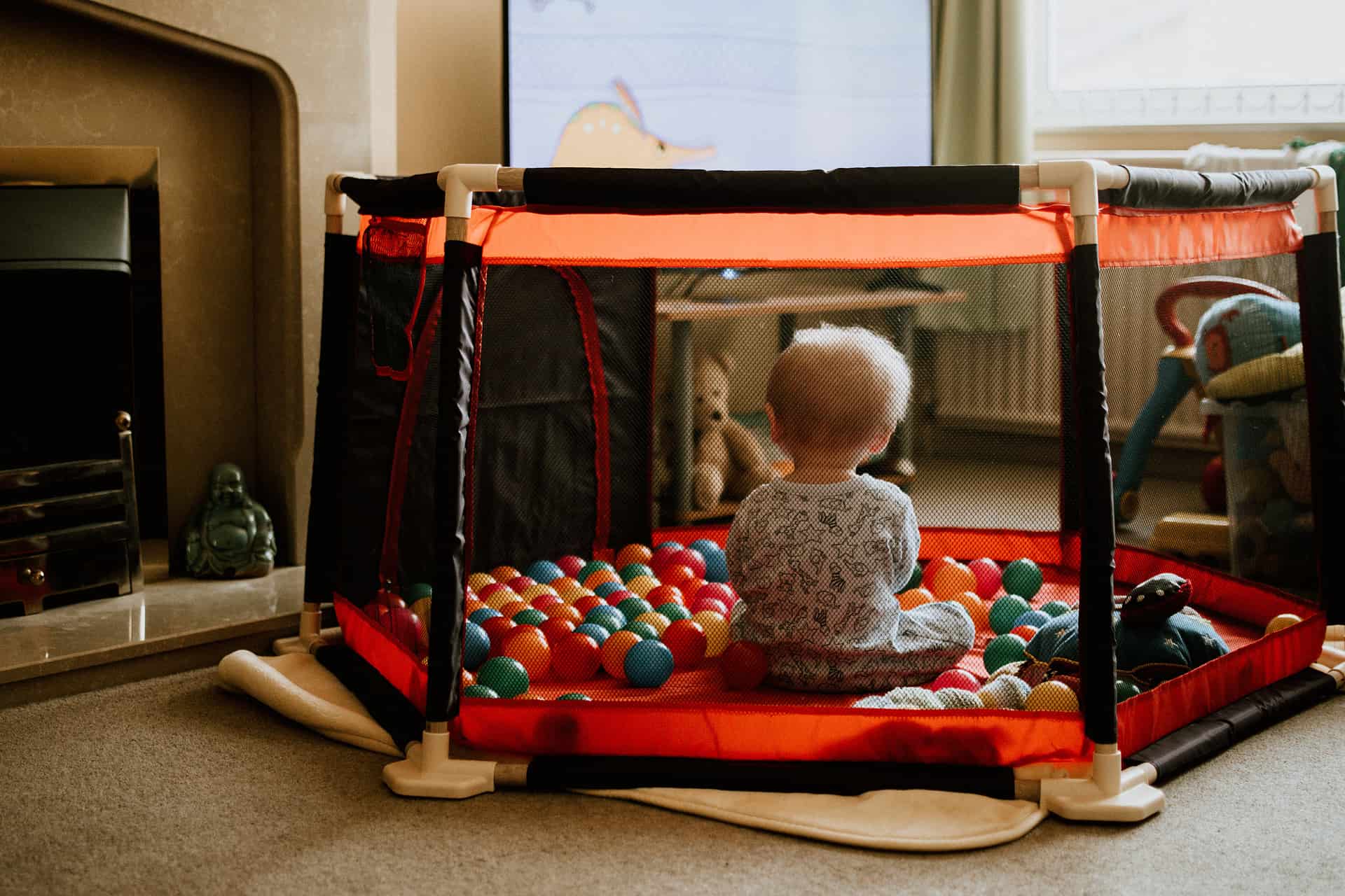A baby sitting inside a fenced play yard on a living room floor